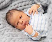 Neugeborenes Baby mit kurzen, dunklen Haaren, das in einem gestreiften Oberteil auf einer grauen Decke liegt.