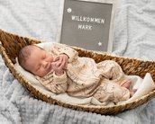 Neugeborenes Baby schläft in einem Korb, umgeben von einer Decke, mit einem Schild, das "Willkommen Mark" zeigt.