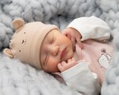 Neugeborenes Baby schläft friedlich in einer weichen Decke, trägt eine Mütze mit Bärenohren und ein rosa Oberteil.