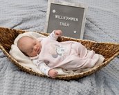 Neugeborenes Baby in einem geflochtenen Korb, trägt einen Schlafanzug mit Minnie-Maus-Motiv. Neben dem Baby steht ein Schild mit "Willkommen Thea".
