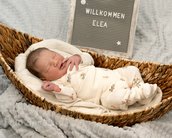 Neugeborenes Baby liegt in einer geflochtenen Wiege, umgeben von einer Decke, mit einem Schild, das "Willkommen Elea" zeigt.