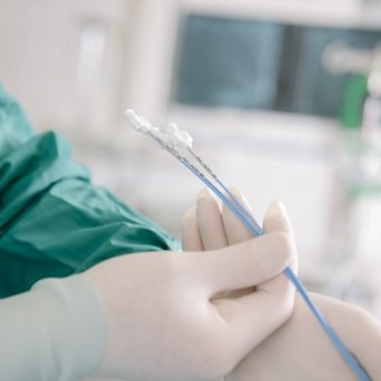 Ein Arzt in grüner OP-Kleidung hält sterile medizinische Instrumente in der Hand, bereit für einen Eingriff.
