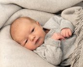 Neugeborenes Baby in einem grauen Pullover, eingekuschelt in eine weiche Decke, mit einem neugierigen Blick.