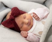 Neugeborenes Baby mit rotem Haarband schläft in einer weichen Decke, trägt einen weißen Overall mit Tiermotiven.