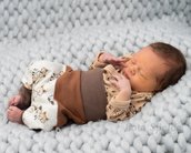 Neugeborenes Baby schläft auf einer grauen Decke, trägt einen gemusterten Oberteil und eine braune Hose.