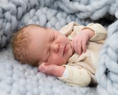 Neugeborenes Baby schläft friedlich in einer weichen, grauen Decke, mit einer Hand an der Wange und der anderen auf dem Bauch.